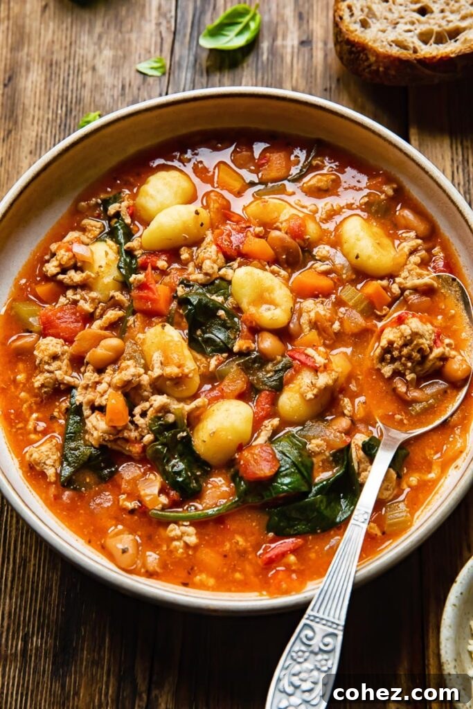 A bowl of Firecracker Sausage Gnocchi Soup with a spoon, showing the rich texture and ingredients.