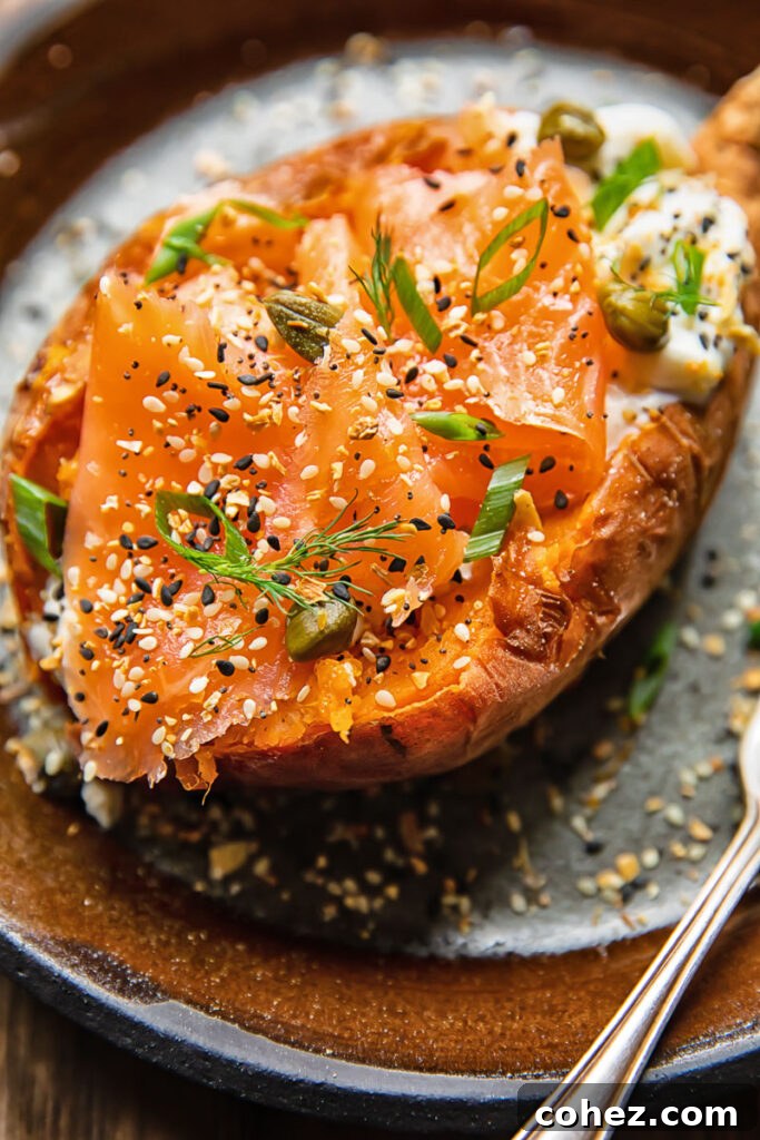 Close-up shot of a baked sweet potato on a plate, generously topped with sour cream, delicate smoked salmon, fresh green onions, and briny capers, embodying a gourmet New York Bagel inspiration.