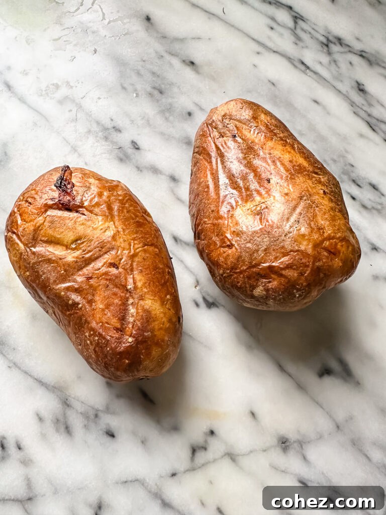 Top-down shot of two perfectly baked potatoes resting on a sleek marble counter, highlighting their inviting, crispy skins.