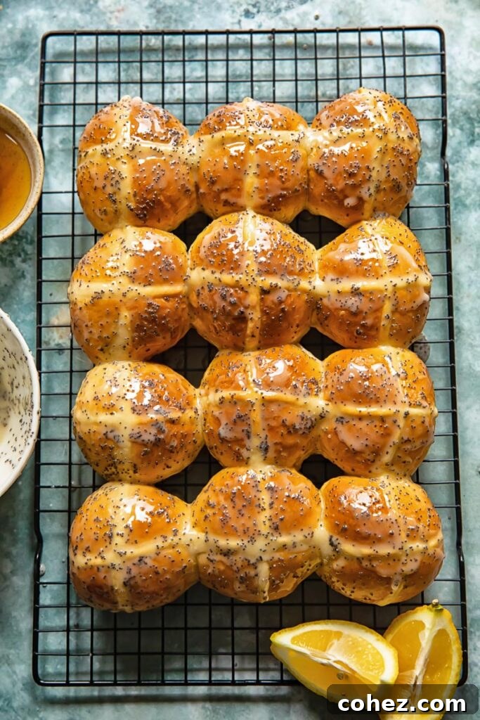 Sunshine Lemon Poppy Seed Hot Cross Buns 5 Freshly baked hot cross buns cooling on a wire rack, garnished with lemon slices.