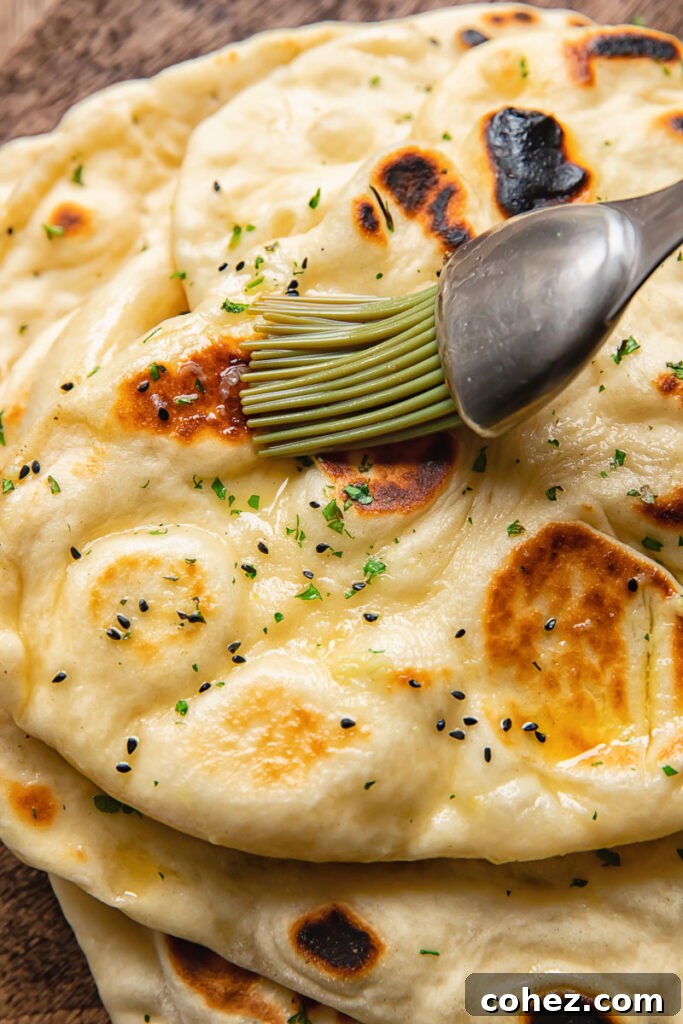 Naan Bread From Scratch 3 Close up shot of warm garlic butter being spread on a homemade naan with a brush