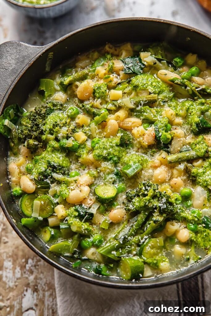 A large pot brimming with vibrant green vegetarian minestrone soup, set against a rustic wooden background.