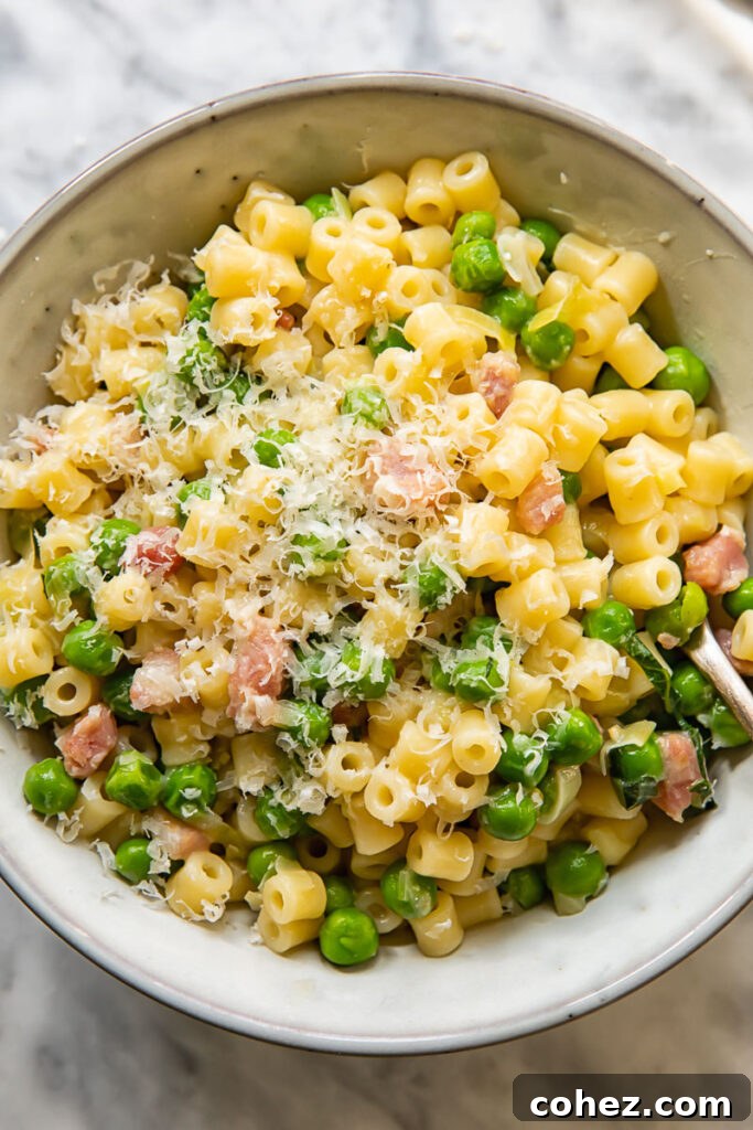 Top down shot of pasta with peas in a bowl topped with grated Parmesan
