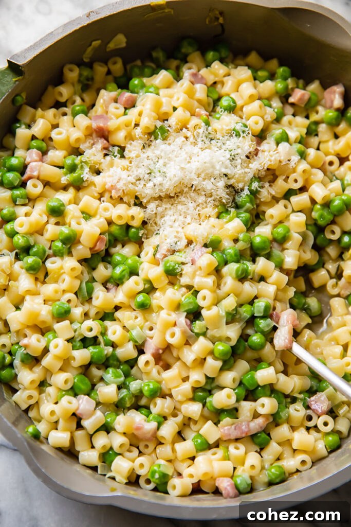 Top down shot of pasta e piselli, with peas and parmesan, being scopped out of a large pan