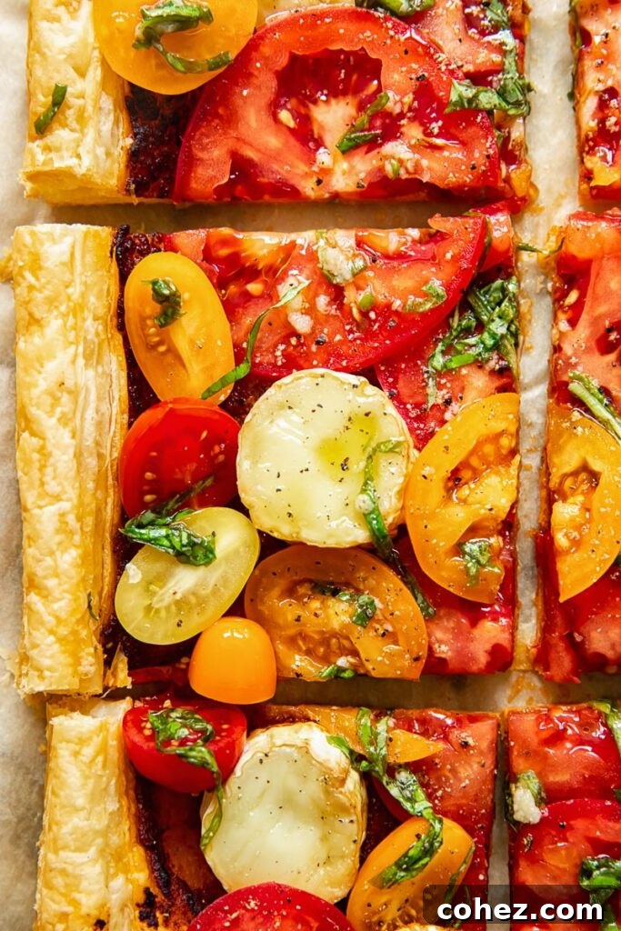 Summer Tomato and Goat Cheese Puff Pastry Tart 2 Close-up of a freshly baked puff pastry tomato tart, showing vibrant slices of heirloom tomatoes, melted goat cheese, and golden-brown pastry.