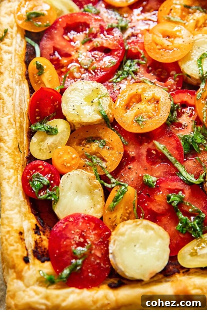 Summer Tomato and Goat Cheese Puff Pastry Tart 6 A close-up of a slice of the puff pastry tomato tart, showing the layered ingredients: flaky crust, pesto, goat cheese, and fresh tomatoes with basil.