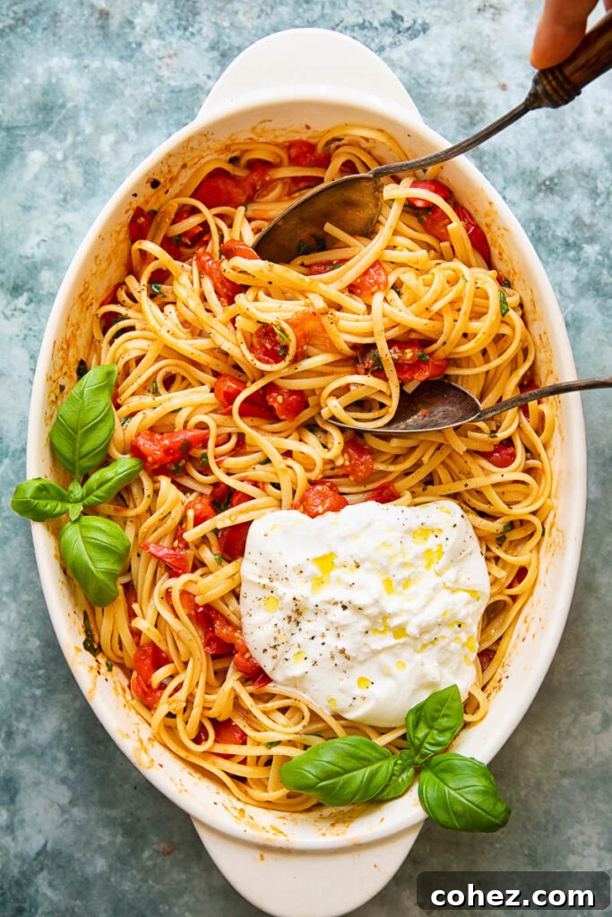 Serving dish with roasted cherry tomato pasta and burrata with serving spoons