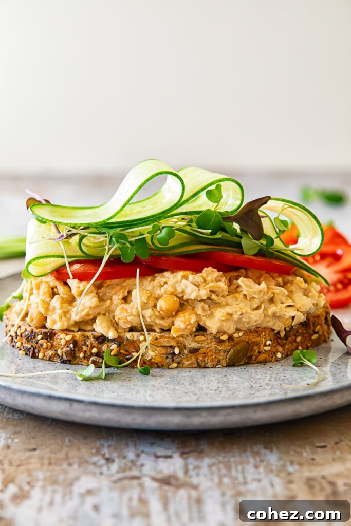 A deliciously prepared chickpea salad sandwich with the top slice of bread slightly ajar, revealing the vibrant, creamy filling and fresh vegetable layers.