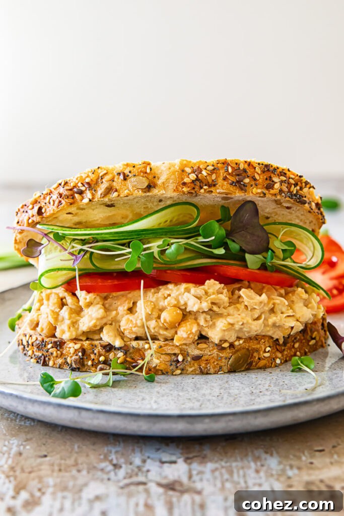 Front view of a chickpea salad sandwich, generously filled with the creamy chickpea mixture and an abundance of fresh vegetables like tomatoes, cucumbers, and microgreens.