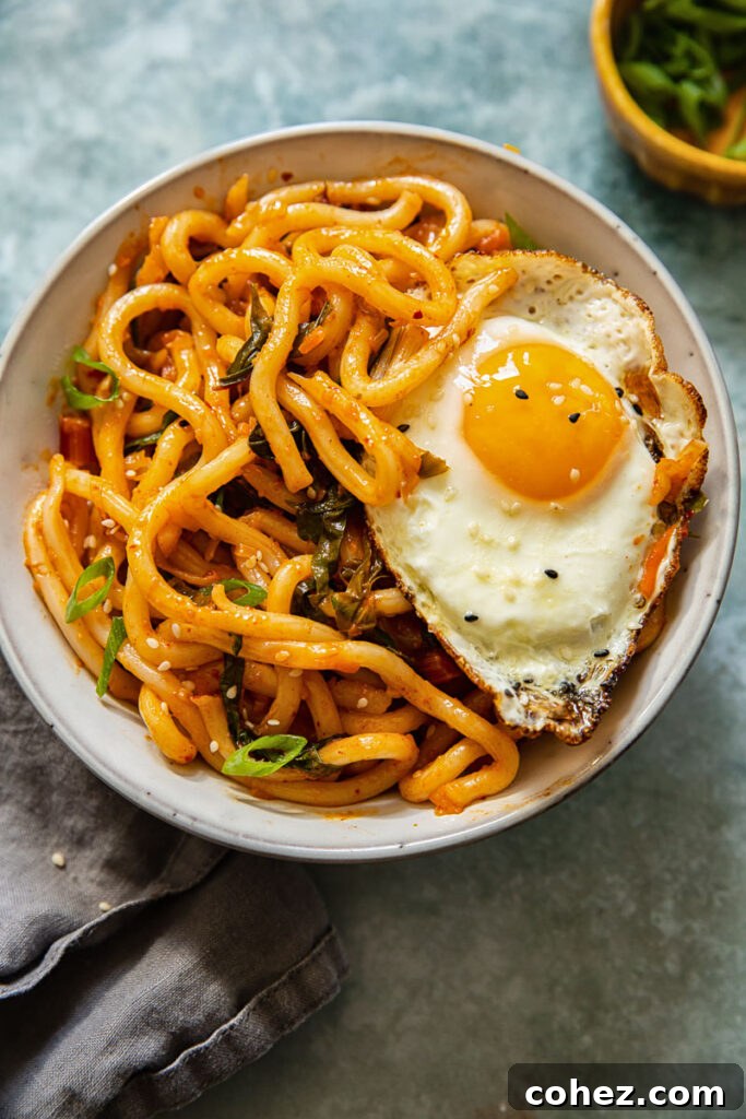 A vibrant bowl of kimchi noodles topped with a perfectly fried egg, ready to be enjoyed with chopsticks.