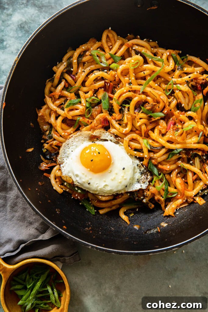 Kimchi noodles simmering in a wok-style pan, with a fried egg being prepared alongside.