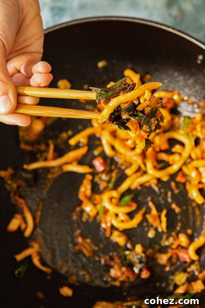 Close-up shot of chopsticks holding a tangle of kimchi noodles, highlighting their texture and the savory sauce.