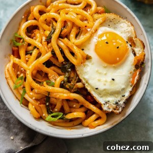 A vibrant bowl of kimchi noodles topped with a perfectly fried egg, ready to be enjoyed.