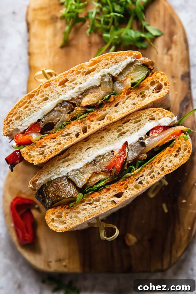 Gourmet Roasted Harvest Vegetable and Chèvre Sandwich 4 Side view of the finished Roasted Vegetable and Goat Cheese Sandwich, cut in half on a wooden cutting board, revealing the layers of filling.