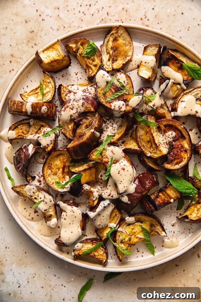 Close up of roasted aubergine on a plate with sauce and mint