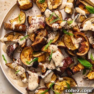Close up of roasted aubergine on a plate with sauce and mint
