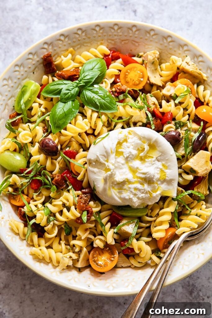 Pasta salad in a bowl with a spoon, showing creamy burrata and colorful vegetables
