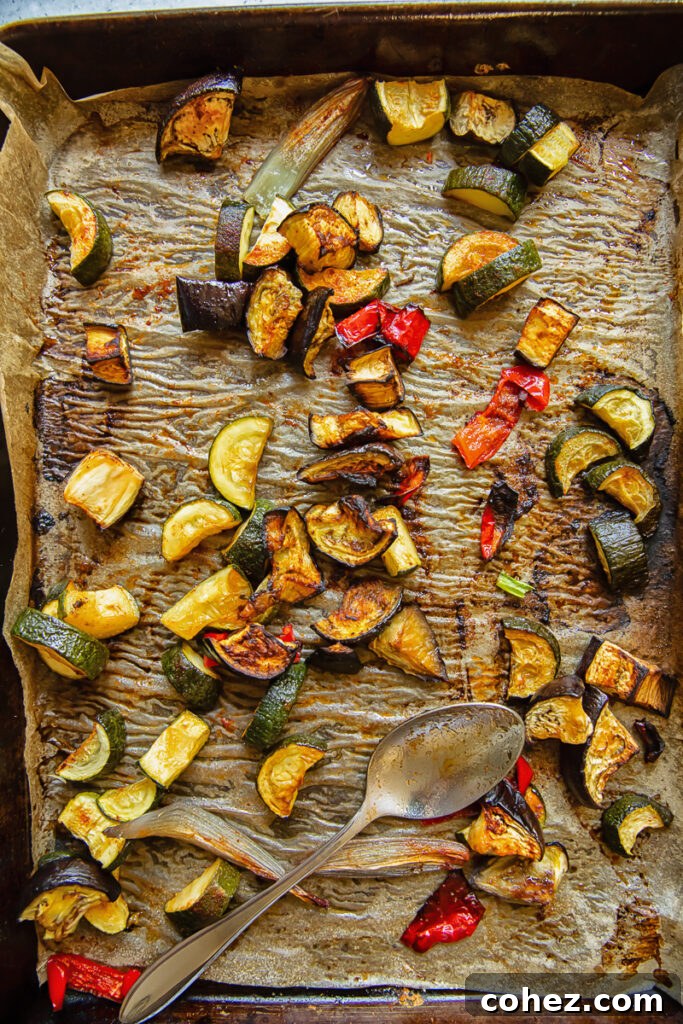 Top down shot of chopped up peppers, eggplant and zucchini roasted on a baking tray