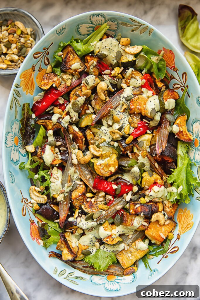 Top down shot of roasted veg salad in a large serving dish topped with nuts and tahini dressing