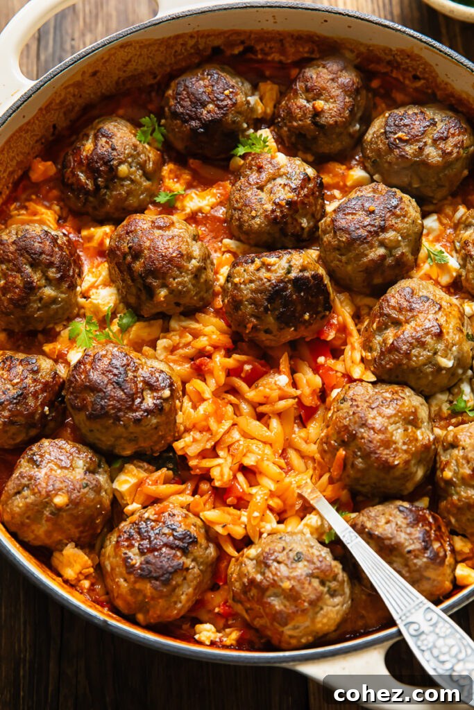 Top down shot of baked orzo being served from a large pan, topped with meatballs