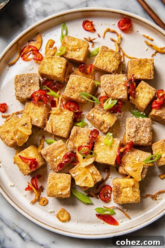 Air fryer tofu bites artfully arranged on a plate with vibrant fried peppers, garlic, and fresh green onions.