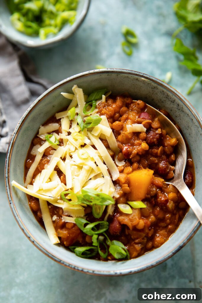A steaming bowl of vibrant vegetarian chili, generously topped with grated cheese and fresh green onions, with a spoon ready for a hearty bite.