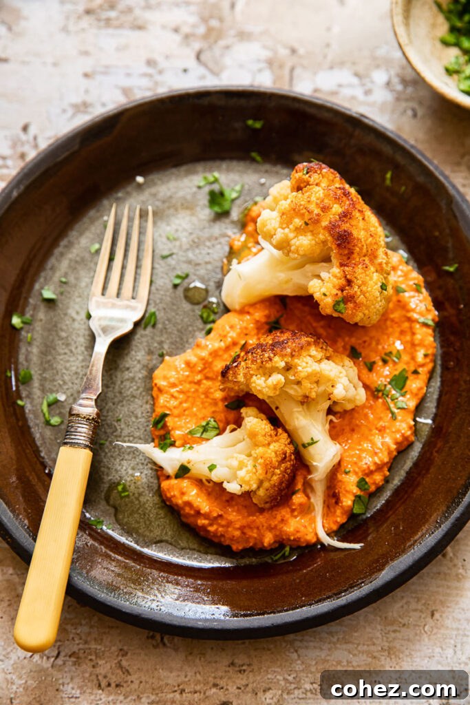 Top down view of a plate of romesco sauce topped with roasted cauliflower florets and a fork