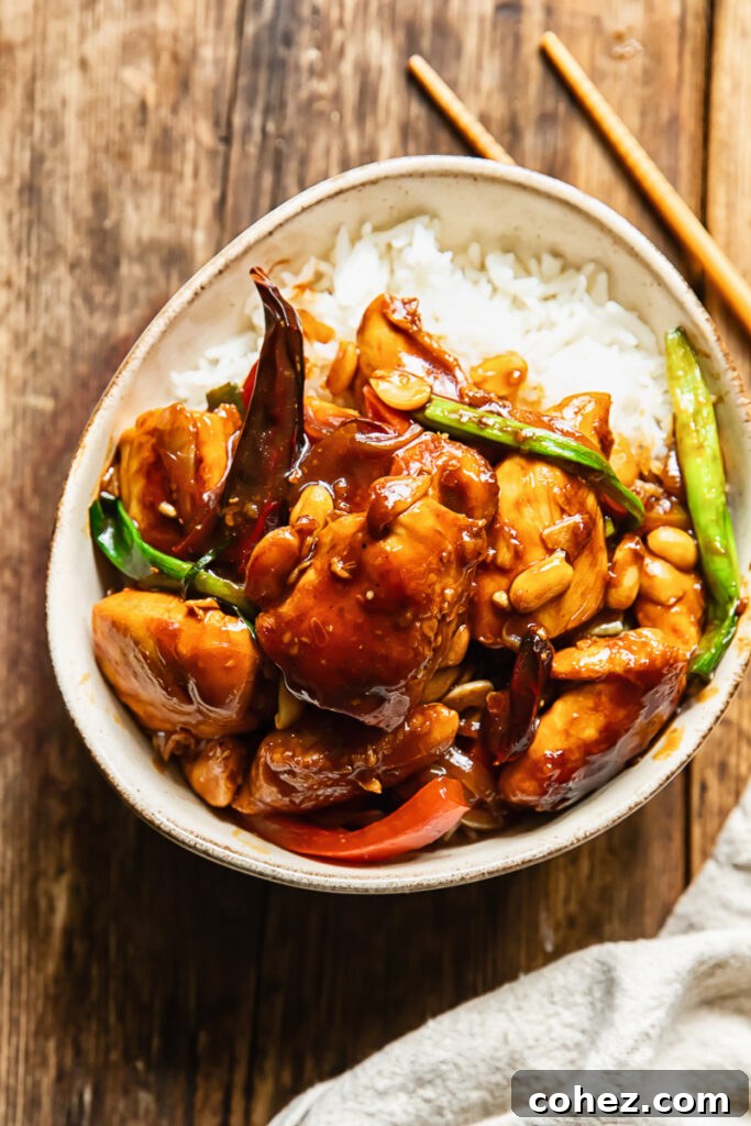 Top down shot of szechuan chicken with green onions and peppers on a bed of rice in a small bowl