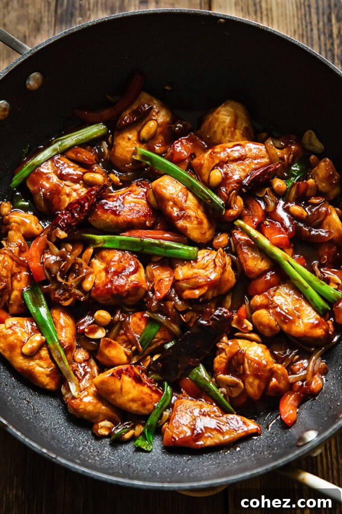 Top down shot of szechuan chicken in a large pan stir fried with green onions and red peppers, topped with peanuts