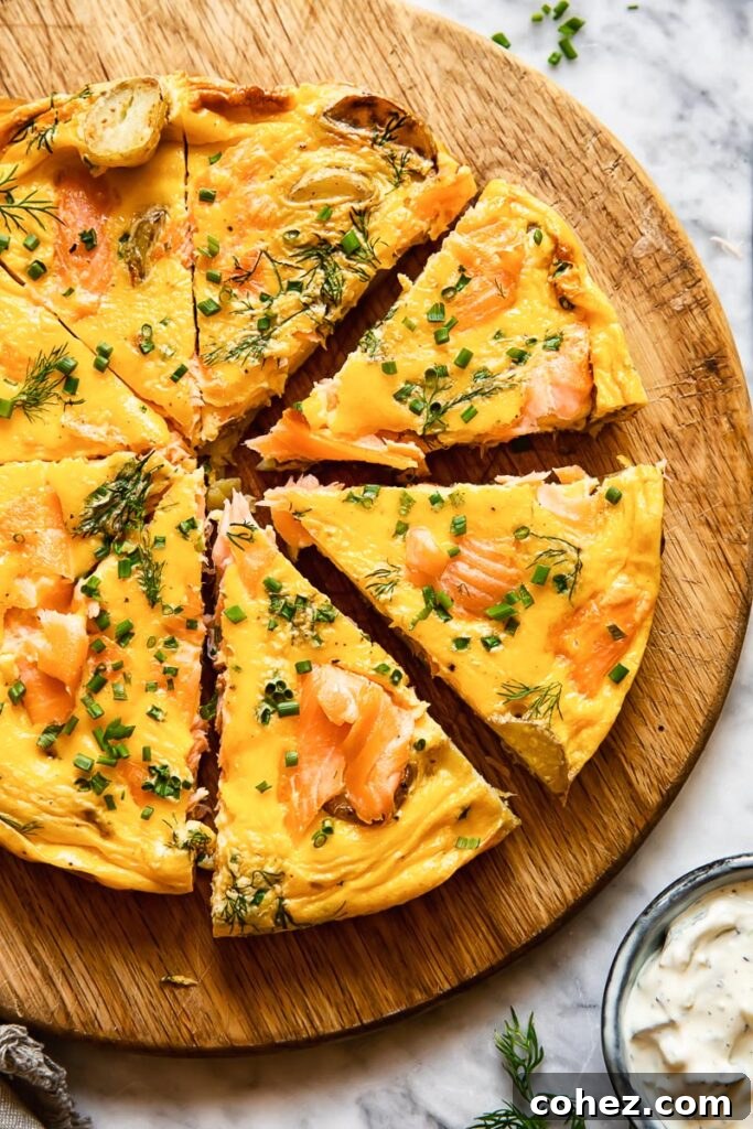 Top down shot of smoked salmon frittata on a cutting board cut into slices and topped with fresh chives