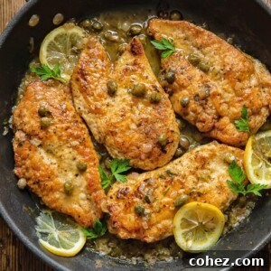 Top down view of chicken breasts in a pan, coated in piccata sauce with lemon slices and capers