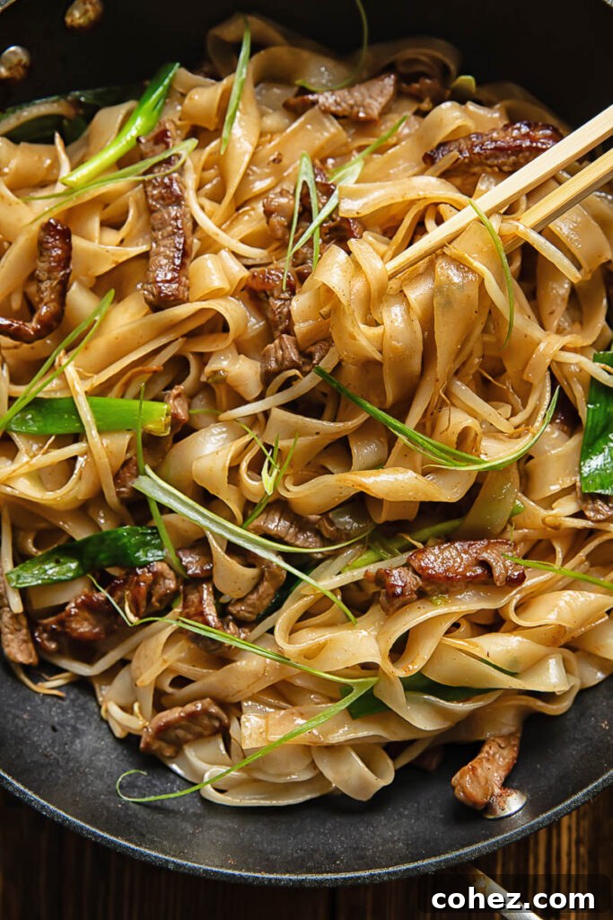 Top down shot of chop sticks picking up chow fun noodles with beef and beansprouts from a pan
