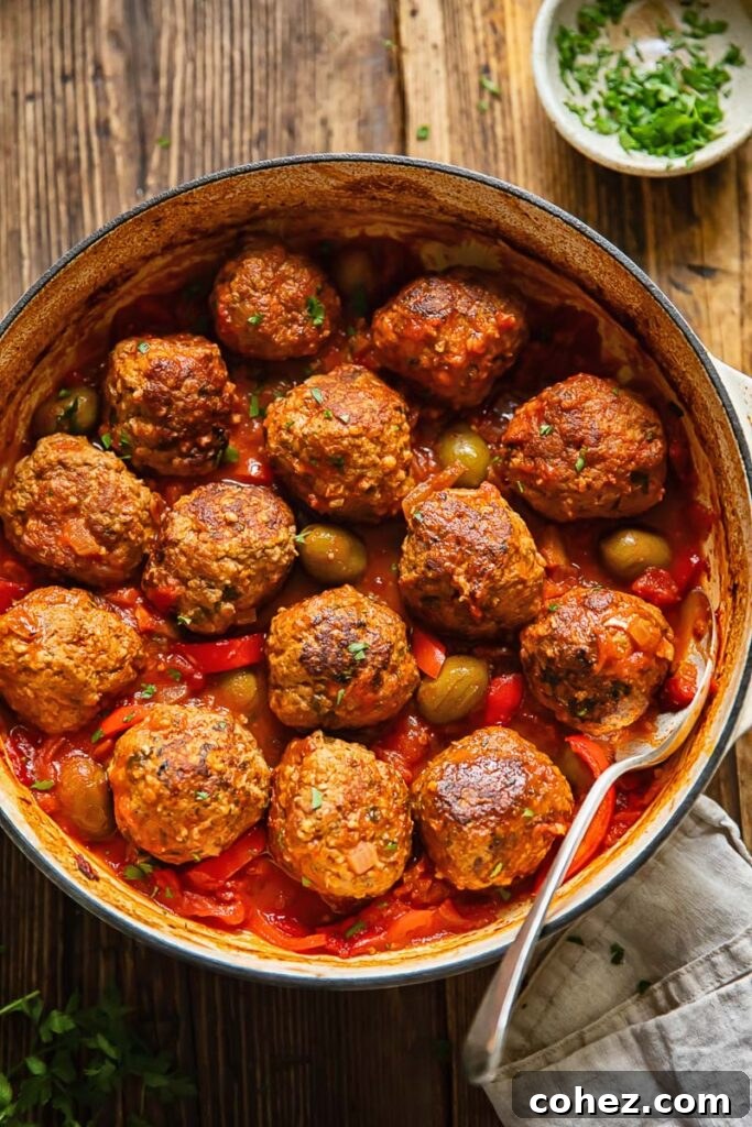 Top down shot of spanish meatballs being scooped out of a pot with olive and tomato sauce
