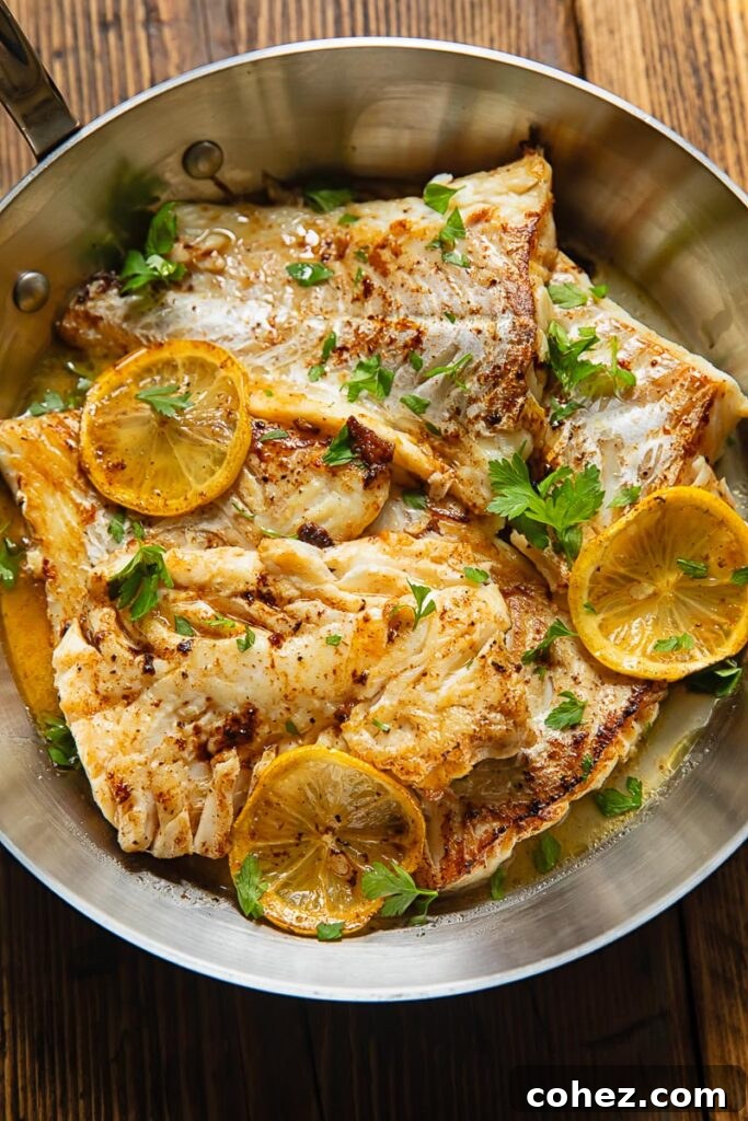 Top-down view of pan-fried lemon butter cod, elegantly garnished with fresh lemon slices and vibrant green parsley, ready to be served from the pan.