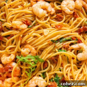 Close up shot of shrimp and spaghetti with sun dried tomato and chilli sauce topped with arugula