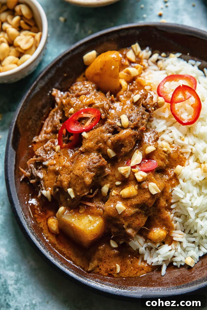 Close up shot of short rib massaman curry in a plate on a bed of rice topped with peanuts and chilli slices