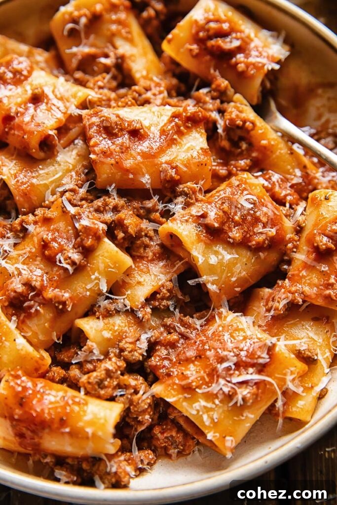Close up shot of paccheri pasta generously coated in a vibrant beef and tomato sauce, infused with 'nduja and topped with freshly grated Parmesan cheese, ready to be enjoyed.