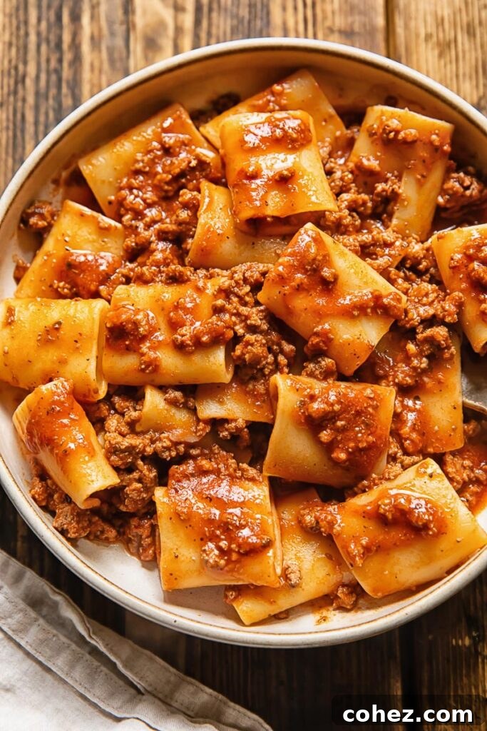 Top down view of a bowl of 'Nduja Beef Tomato Pasta, garnished with grated Parmesan, showcasing the rich, vibrant color of the sauce and the substantial pasta shape.