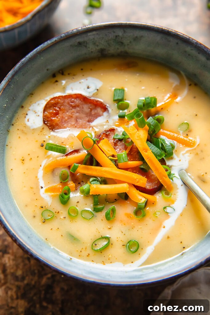 Close up shot of a spoon and bowl of kiebasa potato soup with single cream and herbs