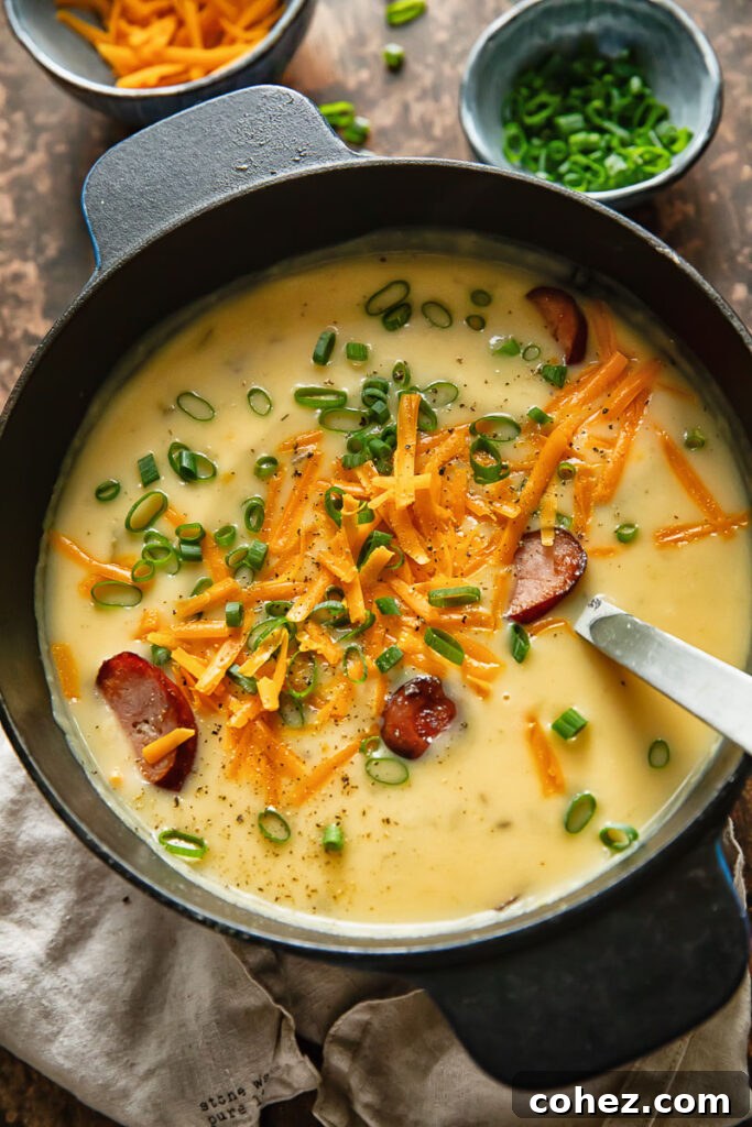 Top down shot of kielbasa potato soup in a pot topped with green onions and grated cheese