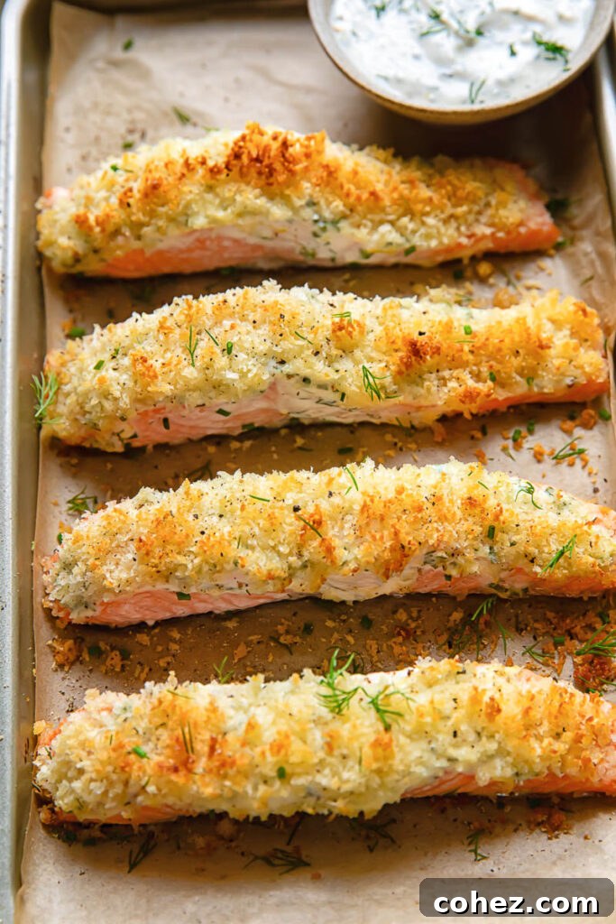 Golden Baked Garlic Herb Salmon with Panko Crunch 4 Top-down shot of multiple garlic baked salmon fillets on a baking sheet, accompanied by a small bowl of the herb and garlic sour cream dip.