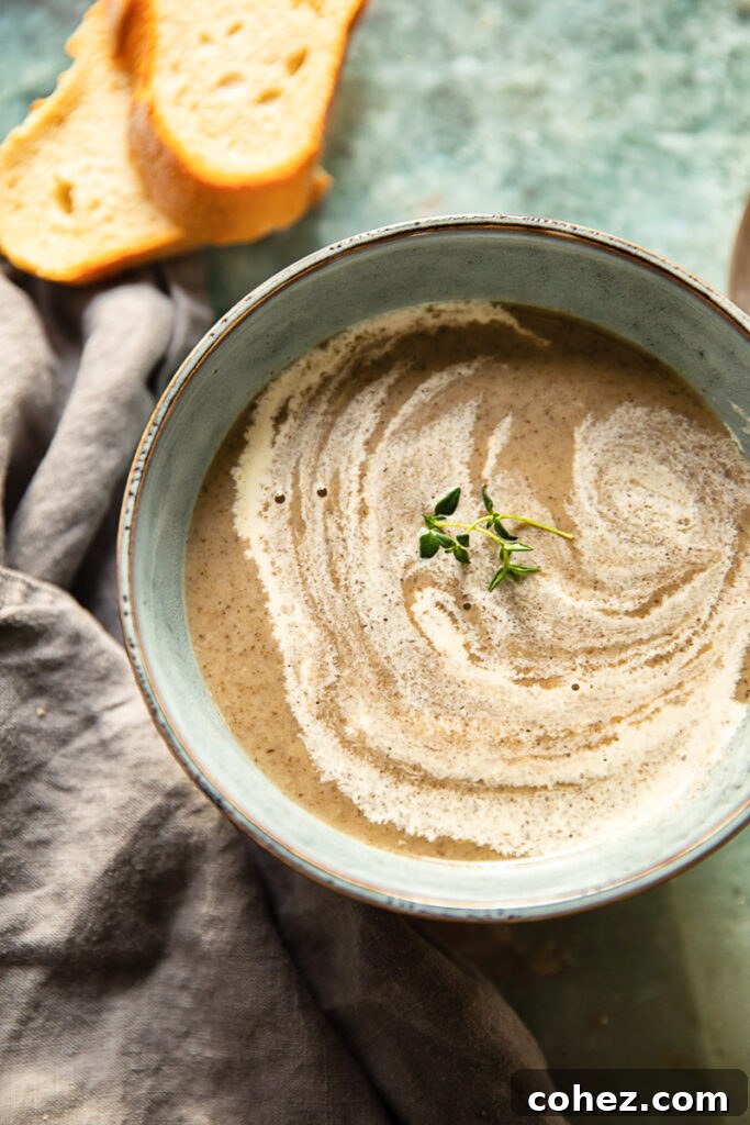 A top-down view of a steaming bowl of homemade Vegan Cream of Mushroom Soup, garnished with fresh herbs, perfect for a cozy meal.