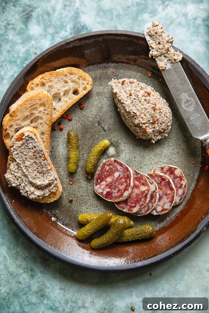 Shot of a plate with mushroom pâté next to slices of bread, gherkins and salami slices