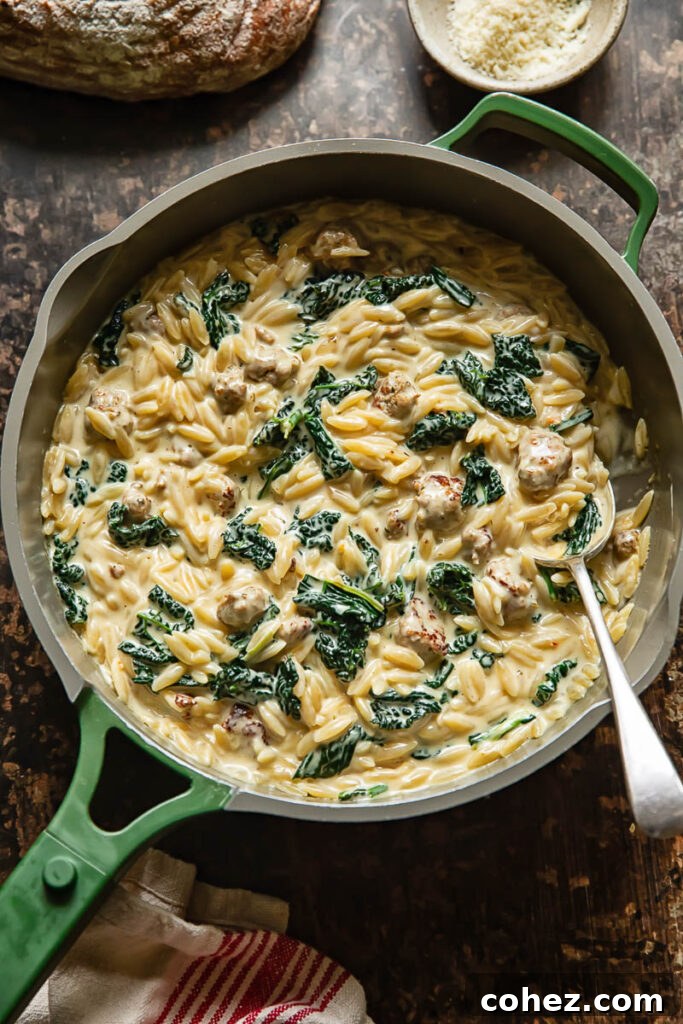 Top down shot of Italian sausage orzo cooking in a wide pan, ingredients are simmering in the rich sauce before the final additions.