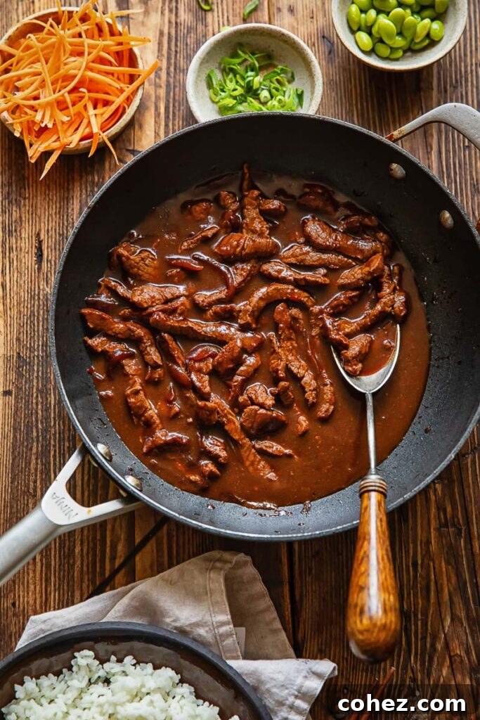 Top down shot of teriyaki beef stir fry in a pan next to bowls of sliced carrot and green onions