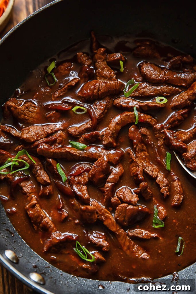 Close up shot of beef teriyaki in a deep wok topped with green onion and sesame seeds