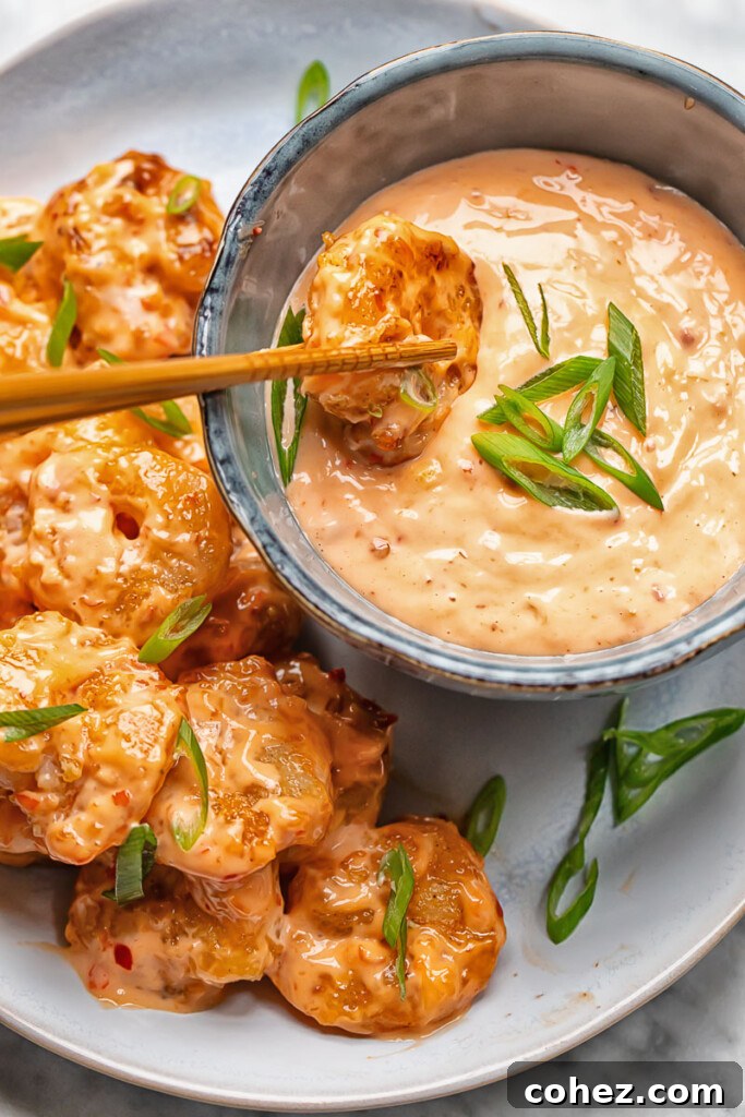 Close up shot of a Bang Bang Shrimp being dipped into a small bowl of spicy mayo sauce, highlighting the rich texture of the sauce.