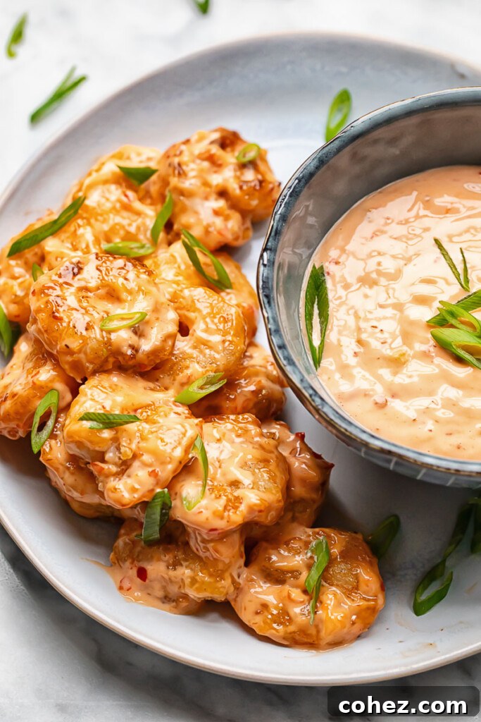 Top down shot of perfectly cooked Bang Bang Shrimp arranged on a white plate, with a small bowl of spicy mayo sauce on the side for dipping.