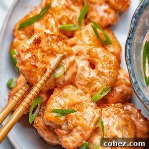 Close up shot of crispy Bang Bang Shrimp being picked up from a plate with chopsticks
