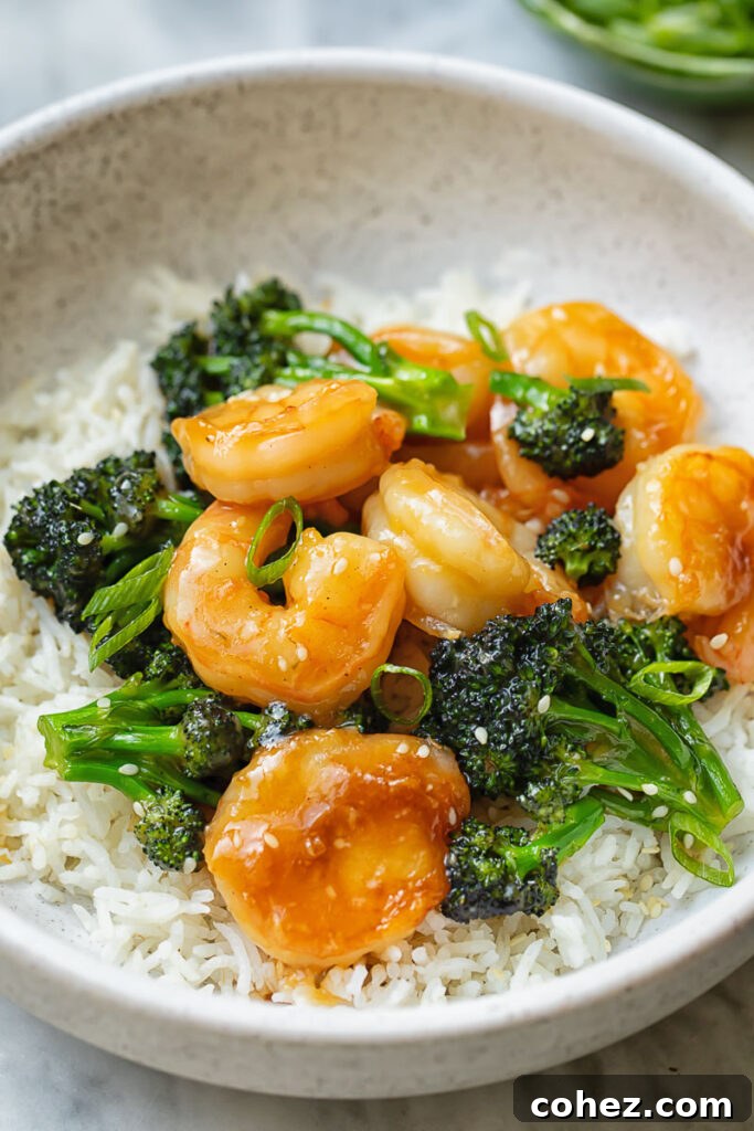 Close up shot of shrimp and broccoli stir fry on top of a bowl of rice, showcasing plump shrimp and vibrant green broccoli.
